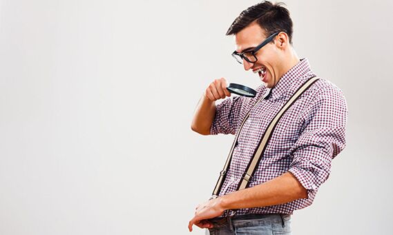 A man looks through a magnifying glass at his penis with the desire to increase its size